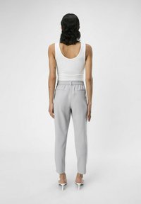 Un débardeur blanc et un pantalon de jogging gris clair avec une taille élastique. Les pantalons ont des poches arrière et des jambes fuselées. Porté avec des sandales à talons transparents.