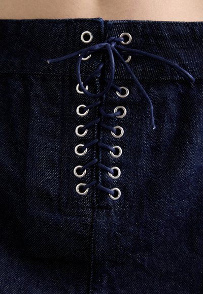 Temno modra denim krila z zasnovo vezanja spredaj, ki vključuje očesca. Tkanina ima subtilno teksturo in gladek zaključek.