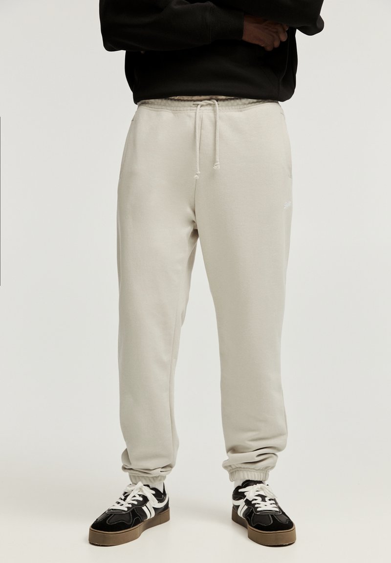 Hellgraue Jogginghose mit elastischem Bund und Bündchen. Hergestellt aus weichem Material, mit Seitentaschen und minimalem Branding.