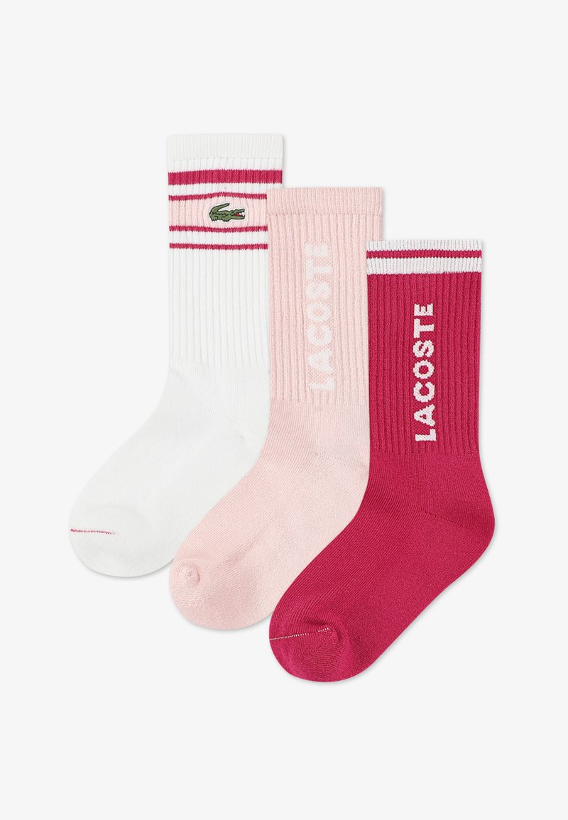 Trois paires de chaussettes : blanches avec des rayures rouges et un logo, rose clair côtelées, et rose foncé avec le logo « LACOSTE », toutes fabriquées en mélange de coton.