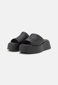 Svart plattform slip-on sko med en vid åpen overdel og glatt lærmateriale. Rund tå, med en tykk og solid såle.