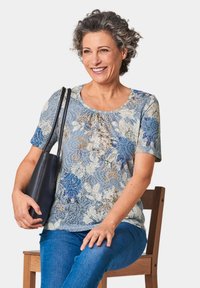 Kurzarmbluse mit floralem Muster in Hellblau und Creme, mit Akzenten in Braun und dunklerem Blau, aus weichem Stoff, Rundhalsausschnitt, entspannte Passform.
