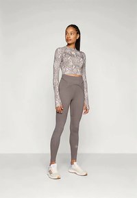 Szary top w wężowy wzór, krótki rękaw, zestawiony z wysokimi, jednolitymi szarymi legginsami i jasnymi butami sportowymi.