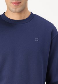 Felpa blu navy realizzata in un tessuto morbido, con colletto rotondo e un piccolo logo di tonalità più scura nella parte sinistra del petto.