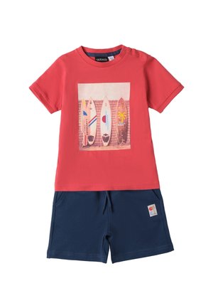 Rotes Baumwoll-T-Shirt mit Surfbrett-Grafik, kombiniert mit marineblauen Shorts mit Seitentaschen und einem Logo-Patch. Klassischer Rundhalsausschnitt, kurze Ärmel.
