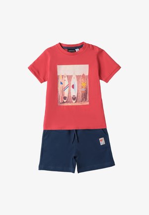 Rotes Baumwoll-T-Shirt mit Surfbrett-Grafik, kombiniert mit marineblauen Shorts mit Seitentaschen und einem Logo-Patch. Klassischer Rundhalsausschnitt, kurze Ärmel.