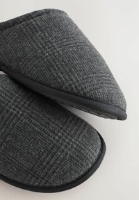 Pantuflas de lana grises con un patrón texturizado, forma curva y suelas de goma negra. El diseño es sencillo y moderno, sin hardware visible.