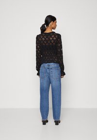 Černý krajkový top s dlouhými rukávy a peplum pasem, spárovaný s modrými džíny s vysokým pasem. Textura je jemná, s květinovým vzorem.