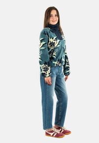 Sudadera de forro polar con estampado floral azul y cuello alto, combinada con jeans de denim holgados y zapatillas rojas con detalles crema y cordones blancos.