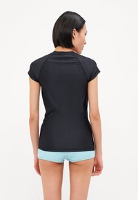 Μαύρη αθλητική μπλούζα κοντό μανίκι με λεία υφή, εφαρμοστό σχέδιο και επίπεδες ραφές, συνδυασμένη με ανοιχτό γαλάζιο σορτς.