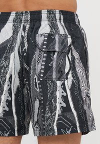 Shorts de bain à motifs noir et blanc avec une taille élastique et une poche latérale dotée d'un rabat et d'une fermeture à pression.