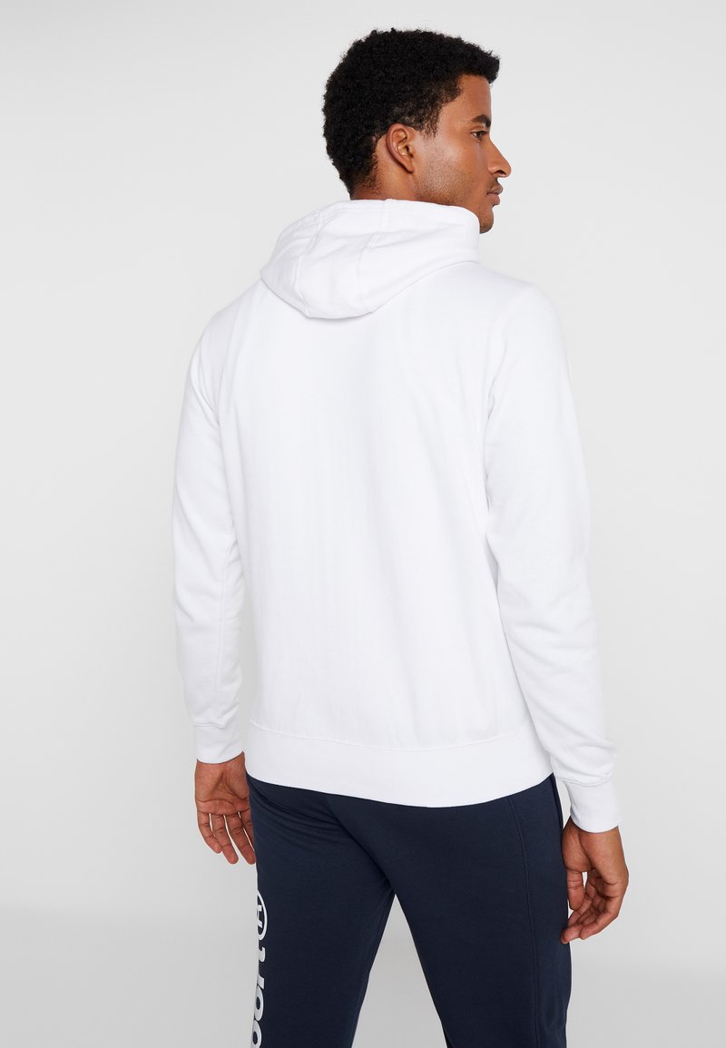 Sudadera blanca con capucha, de manga larga y con un dobladillo acanalado. Textura suave con un diseño minimalista y sin logotipos ni patrones visibles.