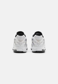 Baltas sporta apavi ar sietu detaļām, sudraba akcentiem un melniem elementiem. Iezīmēts ar mīkstinātu zoli un teksturētu papēža paneli.