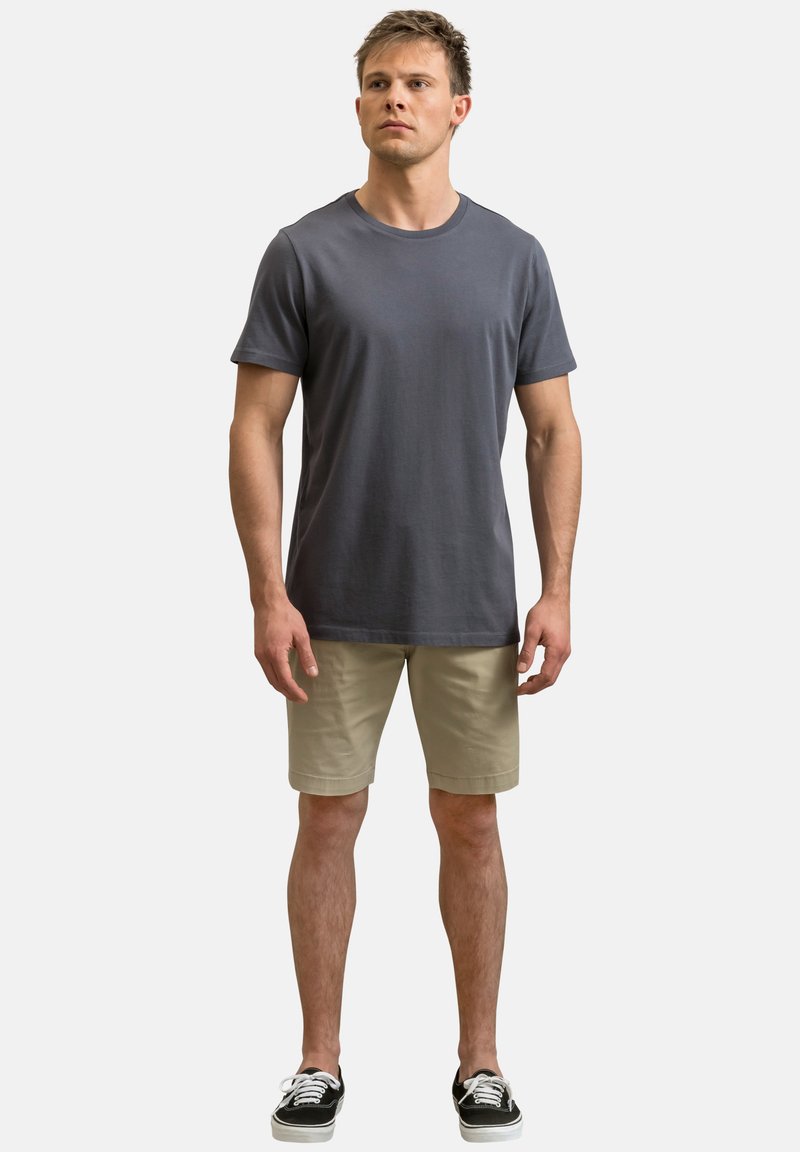 T-shirt en coton gris avec un col rond, assortie à un short beige. La tenue comprend des baskets noires avec des semelles blanches.