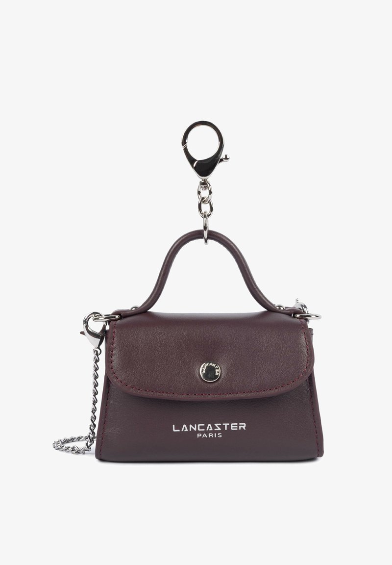 Porte-clés mini sac à main en cuir Lancaster Paris violet foncé avec poignée supérieure, fermeture avant par bouton, et chaîne argentée avec fermoir.