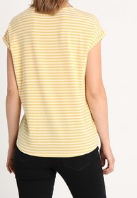 Żółto-biały pasek krótki rękaw top z zaokrąglonym dołem i luźnym krojem, pokazany z tyłu na jednolitym tle.