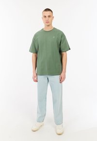 Groene katoenen T-shirt met een ronde hals en korte mouwen, gedragen met lichtblauwe rechte spijkerbroek en witte sneakers.