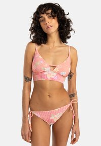 Ružový bikini set s kvetinovými vzormi. Vrchná časť má trojuholníkový tvar a nastaviteľné ramienka; spodná časť obsahuje šnúrky po stranách. Hladká textura.