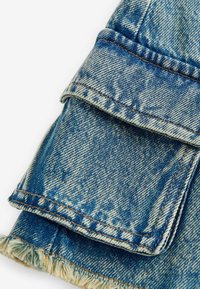 Blå denimtyg med fransad fåll och vikt manschett. Har synlig sömnad och ett mönstrat mönster. Avslappnad och robust design.