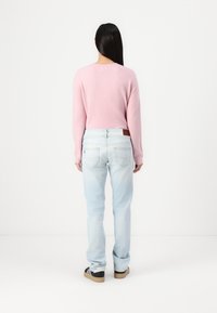 Ανοιχτό ροζ πουλόβερ με μακριά μανίκια, συνδυασμένο με ανοιχτό μπλε τζιν. Η πίσω όψη αποκαλύπτει έναν στρογγυλό λαιμό και μινιμαλιστικό σχέδιο, με επίπεδους ραφές.