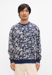 Μπλούζα ναυτικού τύπου με πολύπλοκο λευκό λουλούδι σχέδιο, ριγέ μανίκια και λαιμό. Φτιαγμένη από μαλακό ύφασμα, προσφέρει άνετη εφαρμογή και μακριά μανίκια.