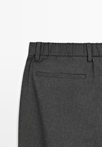Donkergrijze wolachtige broek met een elastische tailleband en een enkele gepaspelde zak aan de achterkant, gezien vanuit het achterste deel van de taille.