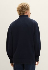 Marineblau gestrickter Pullover mit hohem Kragen, langen Ärmeln, gerippten Bündchen und lockerer Passform. Verfügt über ein strukturiertes Stoffmuster.