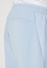 Light blue joggers featuring a smooth fabric with a textured side panel and elastic waistband. Includes a discreet back pocket.