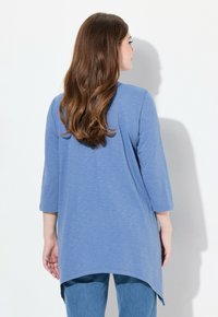 Sinine tunika ümarate krae, kolmanda neljandiku varrukate ja kõrge-maehega. Valmistatud pehmest, tekstureeritud kangast. Sobitatud heledate teksadega.