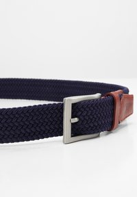 Donkerblauwe gevlochten riem van elastisch materiaal, met een zilveren metalen gesp en bruine leren accenten nabij de gesp.