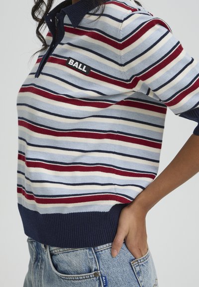 Pull polo rayé en bleu clair, rouge et marine. Il présente un écusson noir avec "BALL", un col côtelé et des poignets. Associé à un short en jean.