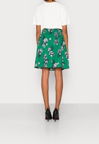 Groene bloemenrok met zwarte bloemenpatronen, elastische tailleband en een luchtig ontwerp. Draag met een witte t-shirt en zwarte hoge hakken.