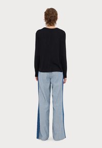 Haut noir à manches longues et jeans larges bleu clair avec des panneaux latéraux bleu foncé. Le tissu semble doux avec une coupe décontractée.