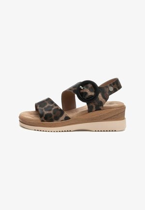 Sandalias de estampado de leopardo con tiras anchas, un acento circular negro y un tacón de cuña con un diseño marrón texturizado y una suela beige.