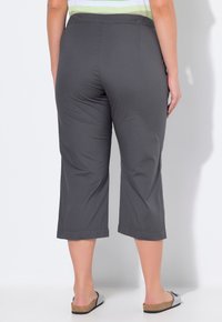 Grijze cropped broek met een elastische tailleband, soepele textuur en eenvoudige zoom, gecombineerd met zilveren slippers op een witte achtergrond.