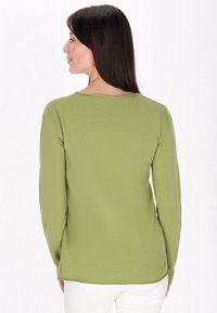 Langsleeve, ronde hals top van zacht, textuurrijk, lichtgroen stof. Heeft een ronde zoom en valt iets onder de heupen.