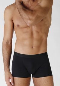 Boxer brevi neri con una texture liscia, vita elastica e un design aderente, modellato secondo la forma del corpo, senza motivi o elementi hardware visibili.