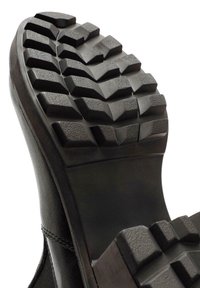 Black rubber boot sole with deep, angular tread patterns. The surface is textured for grip, featuring square and triangular shaped lugs.