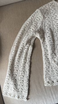 Knit sweater in light beige with openwork pattern, rounded edges, and textured yarn. Long sleeves with decorative lace at the cuffs.