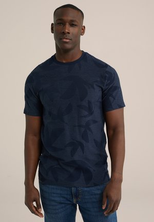 Marineblå t-shirt med et subtilt bladmønster, rund halsudskæring og korte ærmer. Fremstillet af blødt stof og parret med lyseblå jeans.