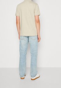 Polo beige en tissu légèrement texturé, associé à un jean droit bleu clair et des baskets blanches avec des semelles marron.