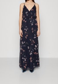 Maxiklänning i mörk marinblått tyg, med ett blommönster i ljusrosa och vitt, med V-ringning och tunna axelband. Framhävd midja.