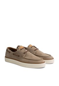 Zapatos de barco de gamuza beige con cordones de cuero, que presentan un diseño perforado y suelas de goma blanca. Detalles cosidos a lo largo de los bordes.