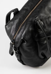 Borsa nera in pelle con forma arrotondata, caratterizzata da una zip in bronzo prominente e una finitura testurizzata. Cinghia regolabile e dettaglio ad anello sul lato.