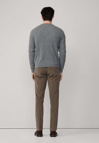 Maglione grigio a trecce con maniche lunghe, scollatura rotonda e orlo a coste abbinato a pantaloni marroni a sigaretta e scarpe scure.