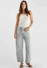 Jean en denim clair à jambes larges avec poches avant et taille à cordon, assorti à un haut blanc sans manches et des sandales marron.