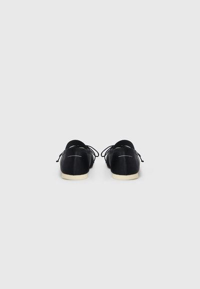 Black shoes with a smooth leather finish, round toe, and white accents. Features laces and a contrasting cream-colored sole.