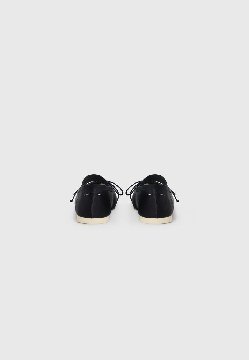 Black shoes with a smooth leather finish, round toe, and white accents. Features laces and a contrasting cream-colored sole.