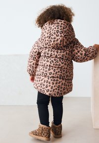 Lyserød dunjakke med sort leopardprint, udstyret med hætte og ribstrikkede manchetter, kombineret med sorte leggings og leopardprint-støvler.