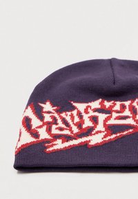 Ciemnofioletowa dziana czapka z daszkiem z czerwonymi i białymi wyraźnymi zygzakowymi literami wyhaftowanymi na przedniej krawędzi.